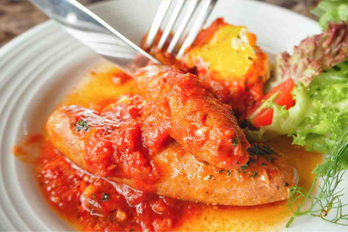 due salsicce al sugo in un piatto tagliate con forchetta e coltello