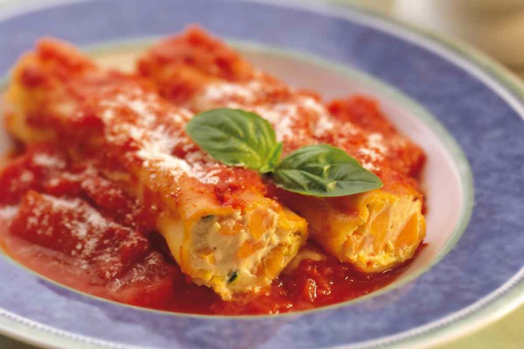 Cannelloni ripieni di carciofi salmone e gamberi conditi con sugo in un piatto