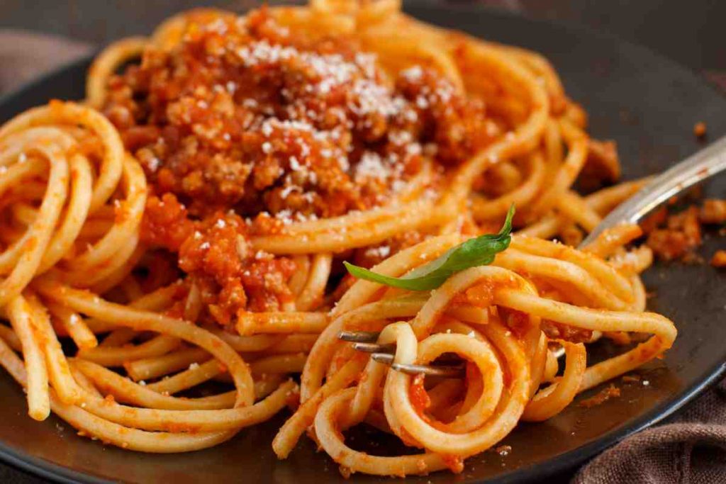 Spaghetti alla chitarra con salsiccia in un piatto nero con una forchetta infilzata