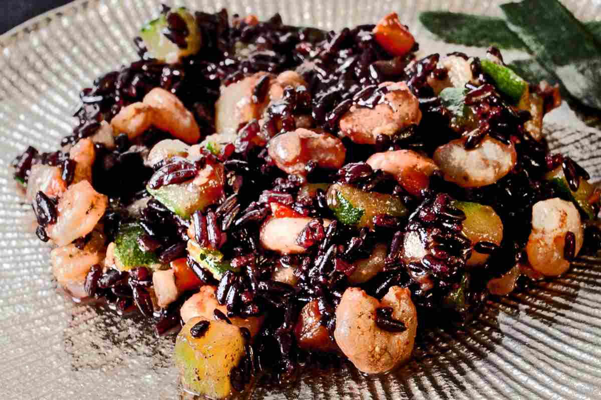 Insalata di riso venere in un piatto di vetro trasparente arricchita con gamberetti, tonno, salmone affumicato e verdure
