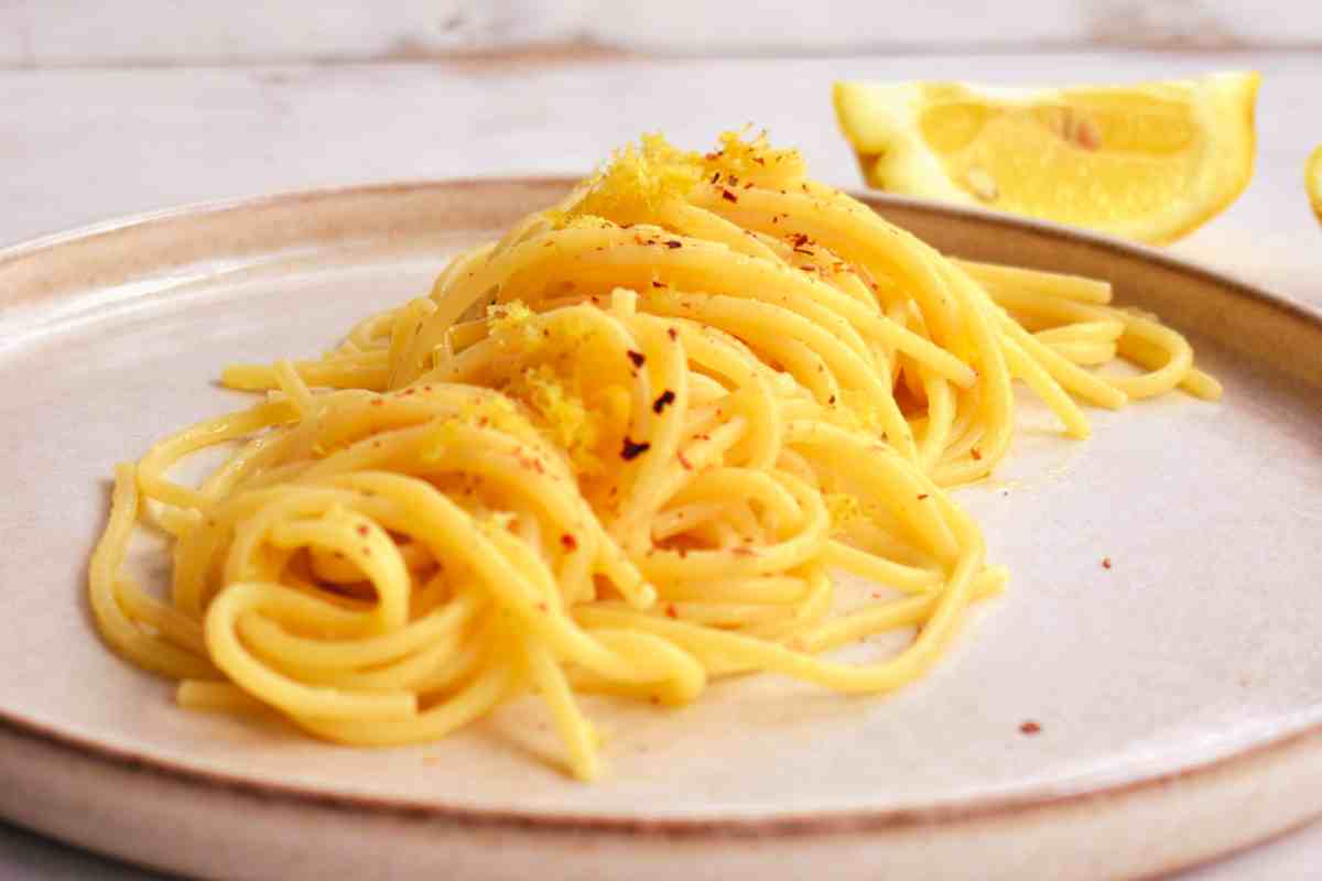 Spaghetti al profumo di limone in un piatto piano con spicchi di limoni sullo sfondo