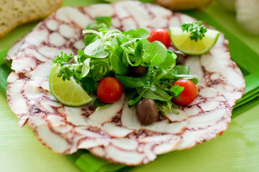 Carpaccio di polpo in un piatto con pomodorini e olive