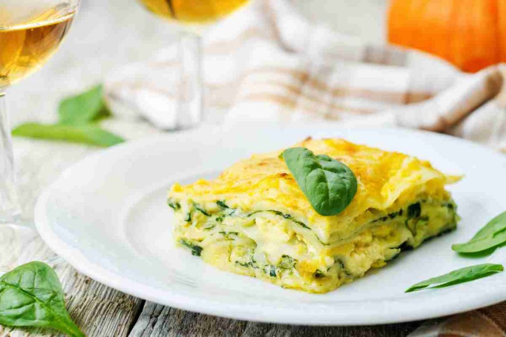 Lasagna con spinaci, scamorza e besciamella su piatto bianco