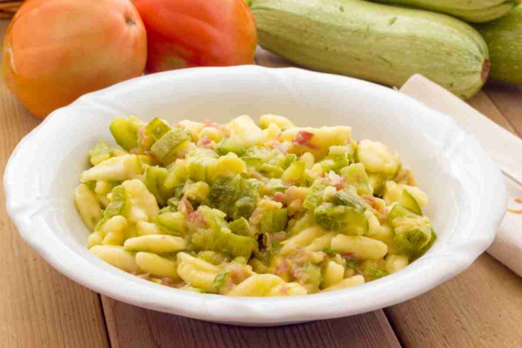 Cavatelli con zucchine e pancetta in un piatto bianco e zucchine crude sul fondo