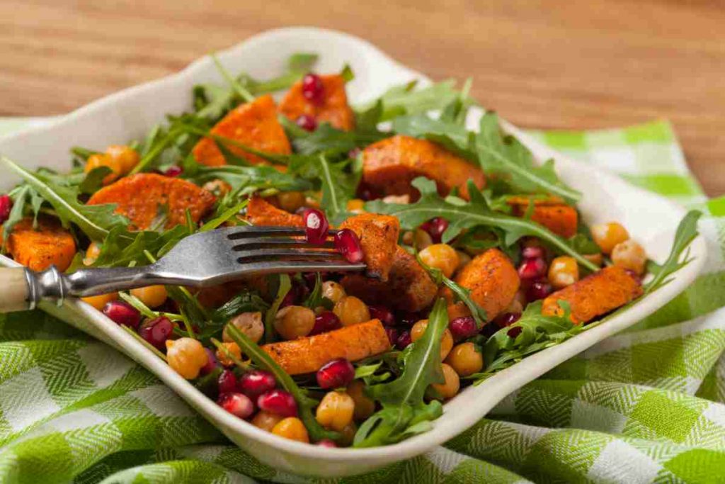 Piatto quadrato con insalata di patate dolci con ceci rucola e melograno 