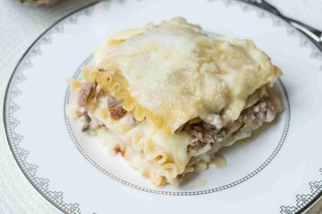 porzione di lasagna bianca carciofi e salsiccia su piatto piano 