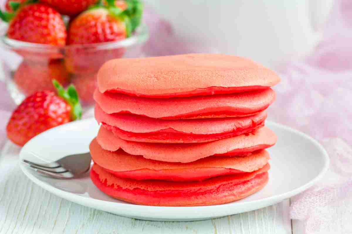 Pancake Red Velvet impilati su un piatto e fragole sullo sfondo