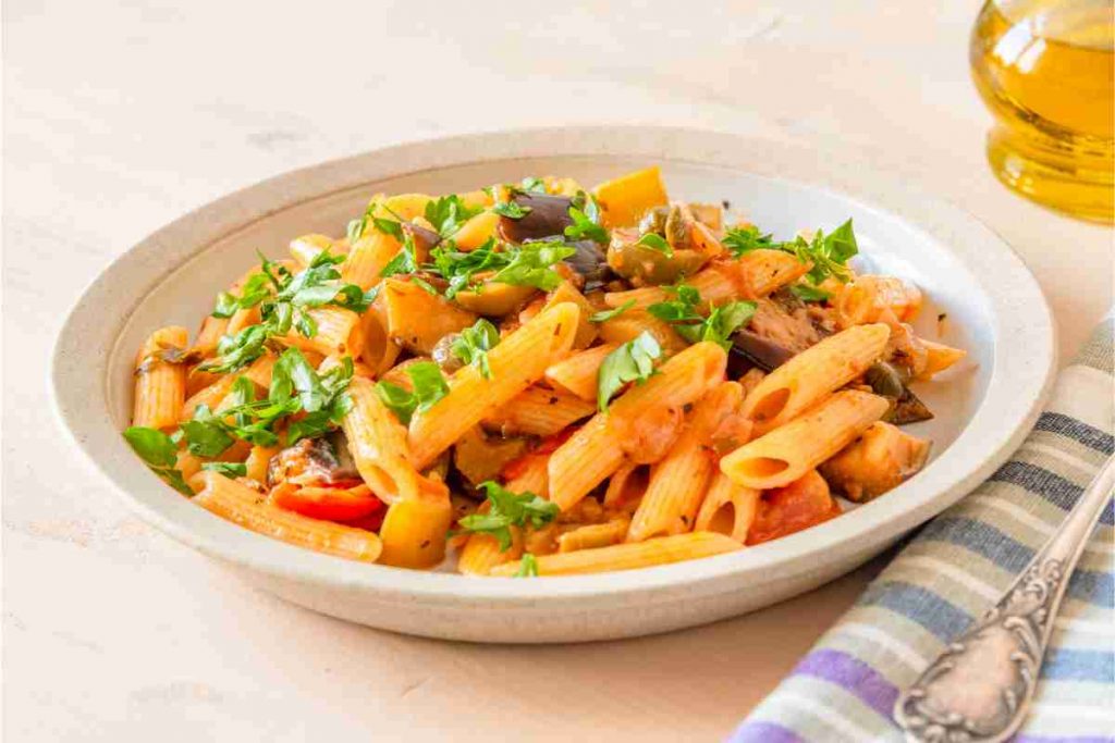 Pasta con caponata in un piatto fondo spolverata con prezzemolo tritato