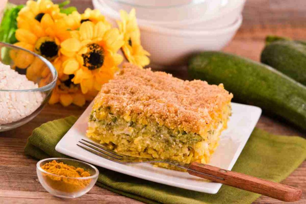 piatto quadrato con del timballo di riso e zucchine con dietro dei fiori gialli