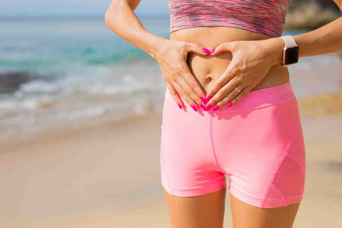 Ragazza vestita di rosa che passeggiando in spiaggia si tocca la pancia