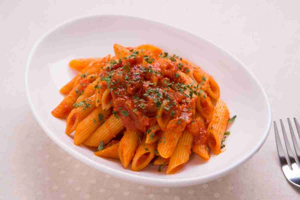 Mezze penne rigate all'arrabbiata con prezzemolo in un piatto bianco