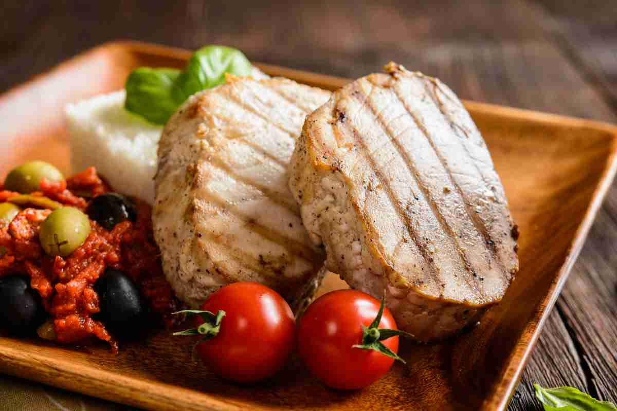 Tonno alla piastra in un piatto con pomodori, salsa alle olive e riso bianco