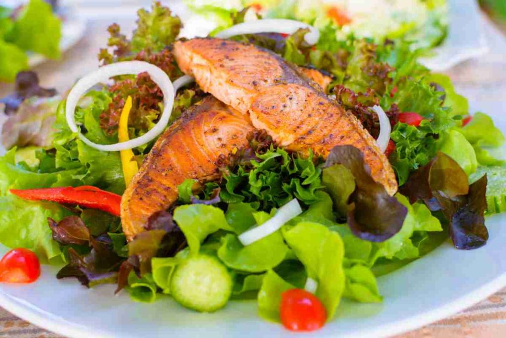Insalata con salmone estiva in un piatto arricchita con cipolla, lattuga e pomodori