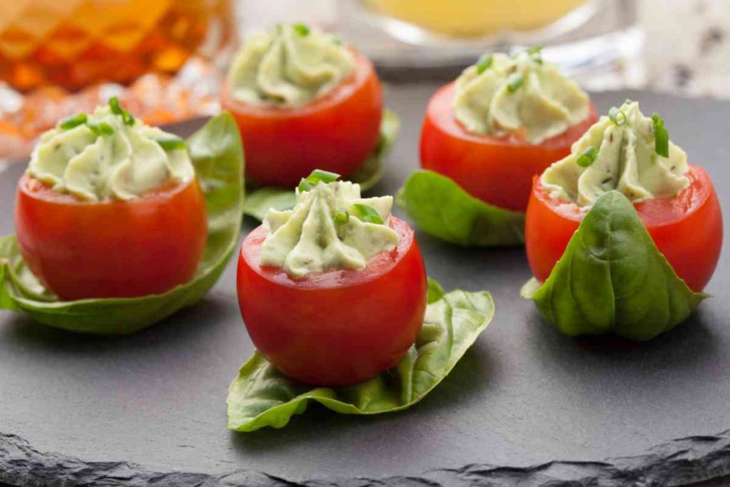 Pomodori freddi ripieni di avocado con sotto una foglia di basilico su un vassoio in ardesia