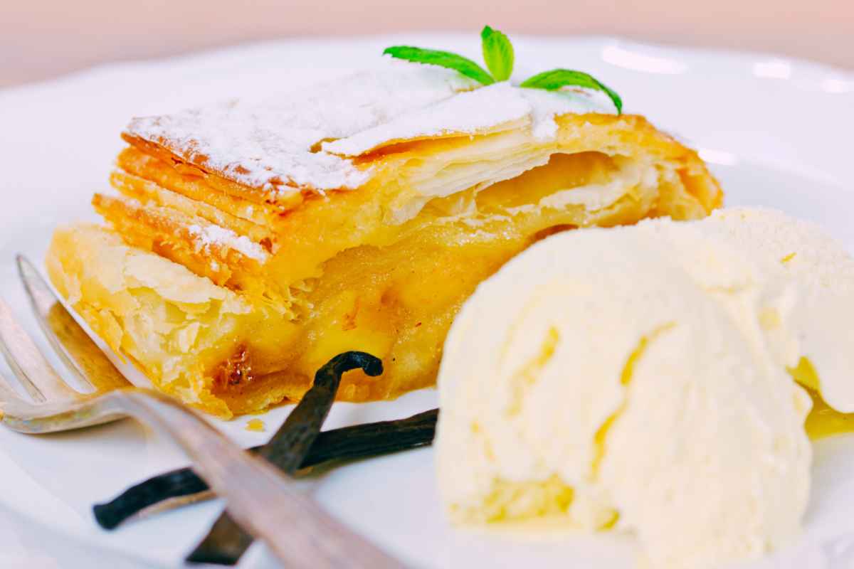 fetta di strudel estivo con pesche e albicocche in un piatto con una pallina di gelato alla vaniglia