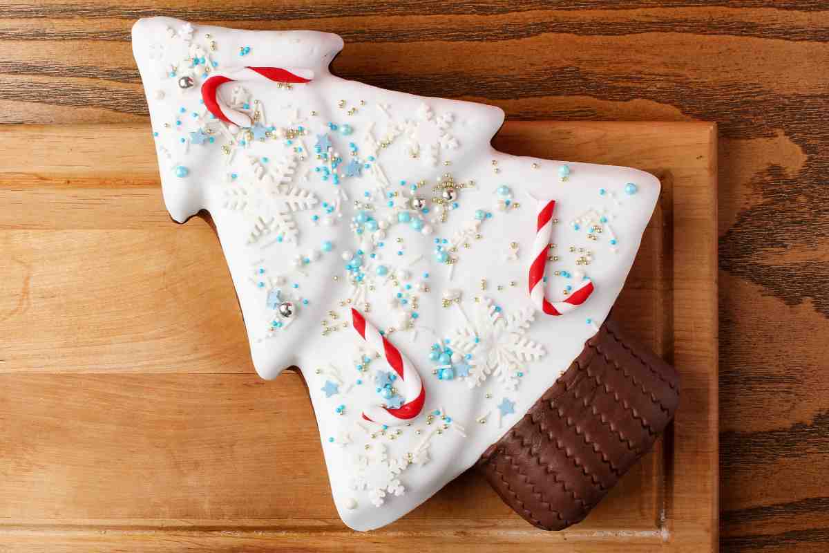 Torta a forma di albero di Natale coperta con pasta di zucchero e decorata con bastoncini bianchi e rossi su un tagliere