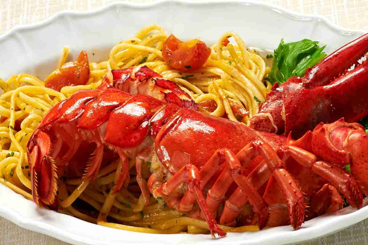 un piatto con una porzione abbondante di linguine condite con sugo all'astice e un crostaceo sopra in bella mostra