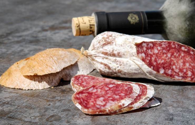 salame con accanto del pane e dietro una bottiglia di vino
