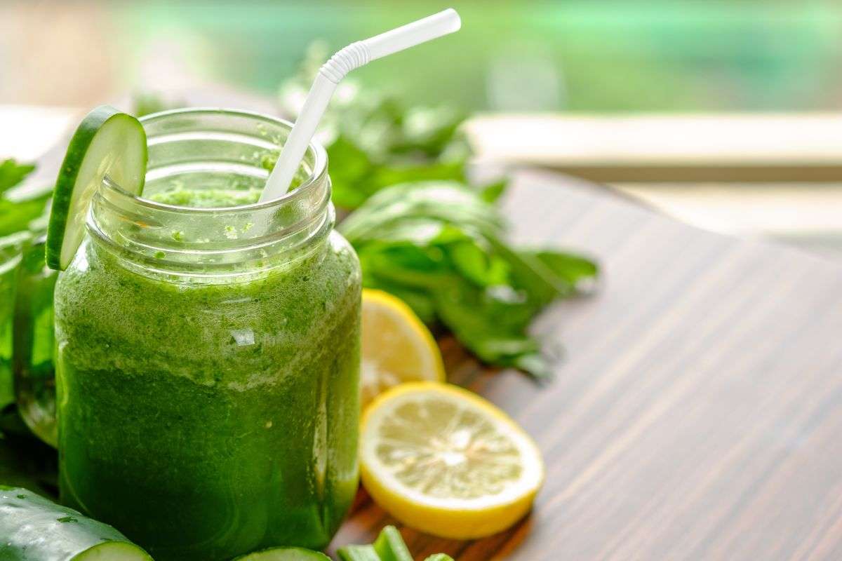 Succo collocato dentro un bicchiere e sul tavolo limone sedano e cetriolo
