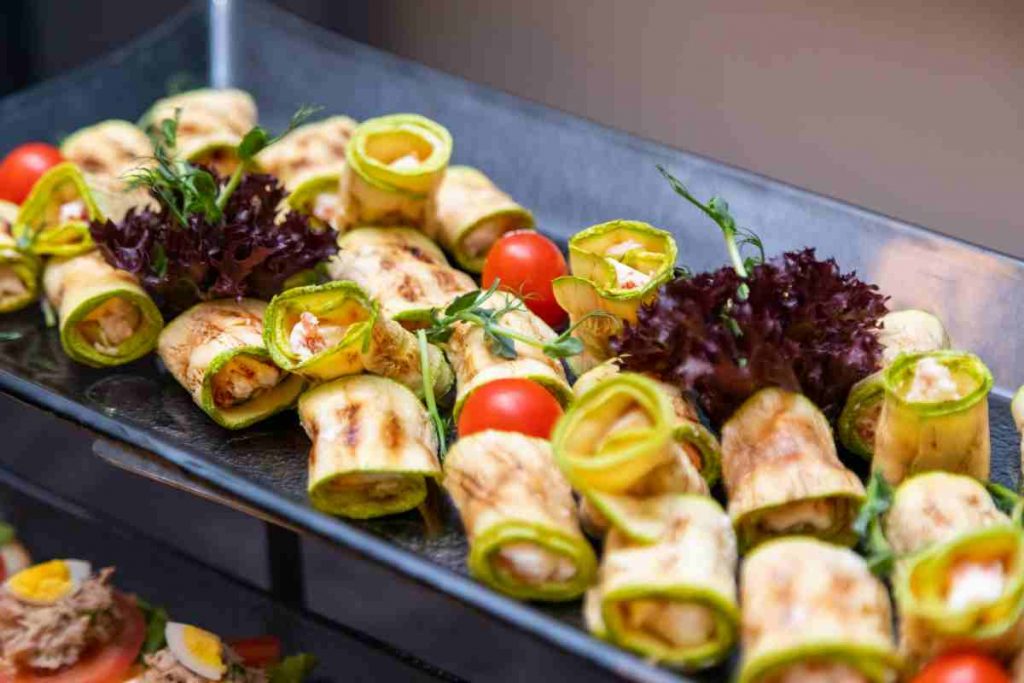 Involtini di zucchine grigliate freddi su un piatto con pomodori e foglie di insalata