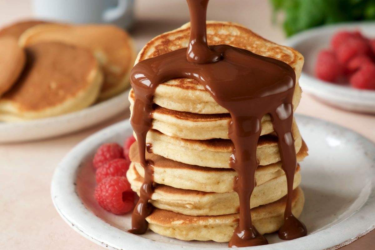 Pancakes impilati e collocati su un piatto, frutta fresca e cioccolato fuso