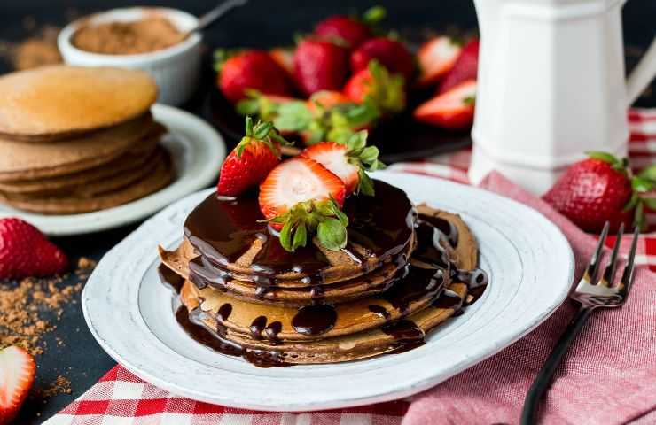 Pancakes impilati adagiati su un piatto fragole e cioccolato fuso sopra