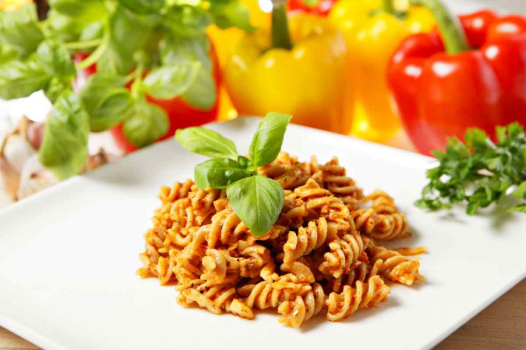 Pasta con pesto di peperoni in un piatto e ortaggi sullo sfondo