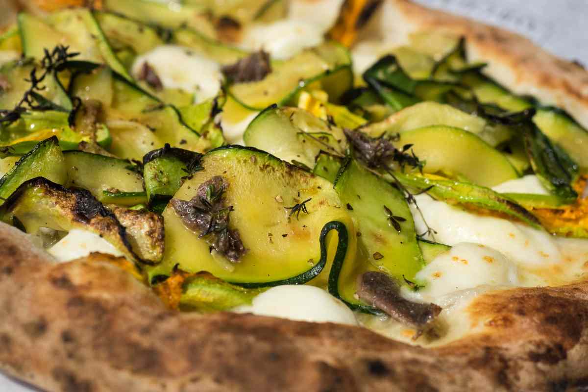 Primo piano di una pizza con zucchine burrata e alici