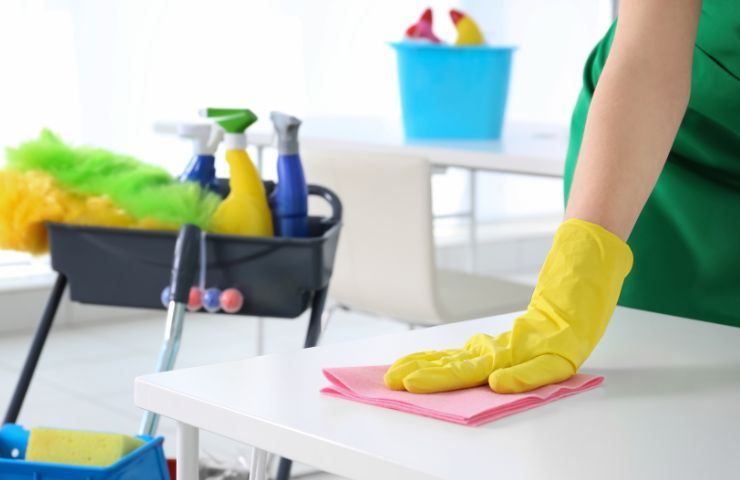 Persona che pulisce con un panno rosa e altri prodotti pensati per le faccende domestiche