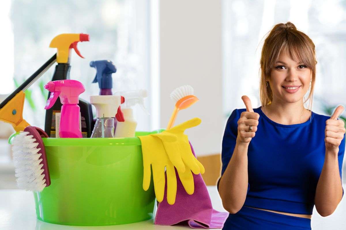 Prodotti e oggetti per la pulizia della casa collocati dentro un secchio e una donna vestita di blu sorridente