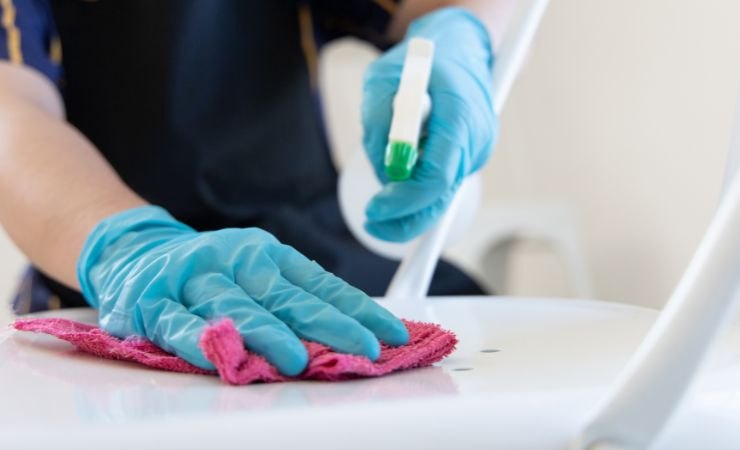 Persona che sta pulendo una superficie in mano tiene il prodotto da utilizzare e un panno