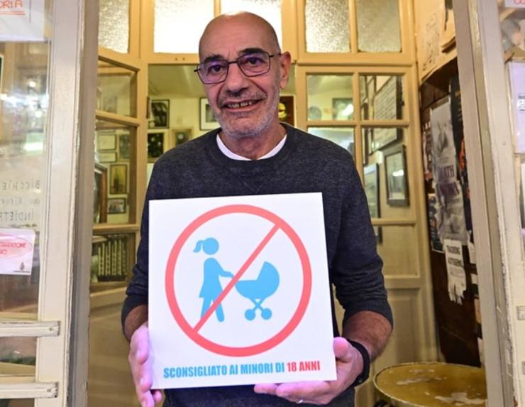 ristoratore con in mano un cartello in cui segnala il divieto di ingresso ai minori di 18 anni