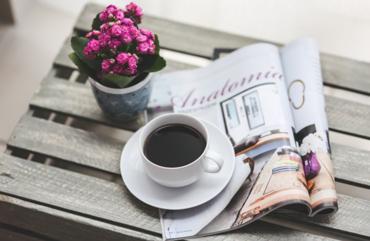 tazzina di caffè su un tavolino con accanto un giornale e una pianta