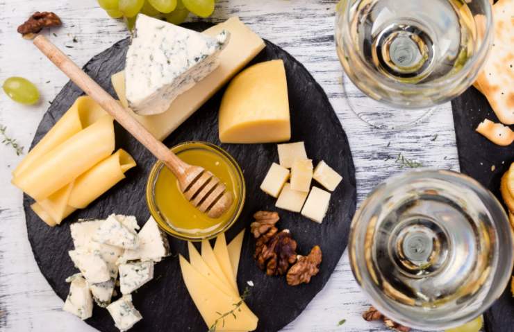 tagliere con sopra formaggi e miele e accanto due calici di vino bianco