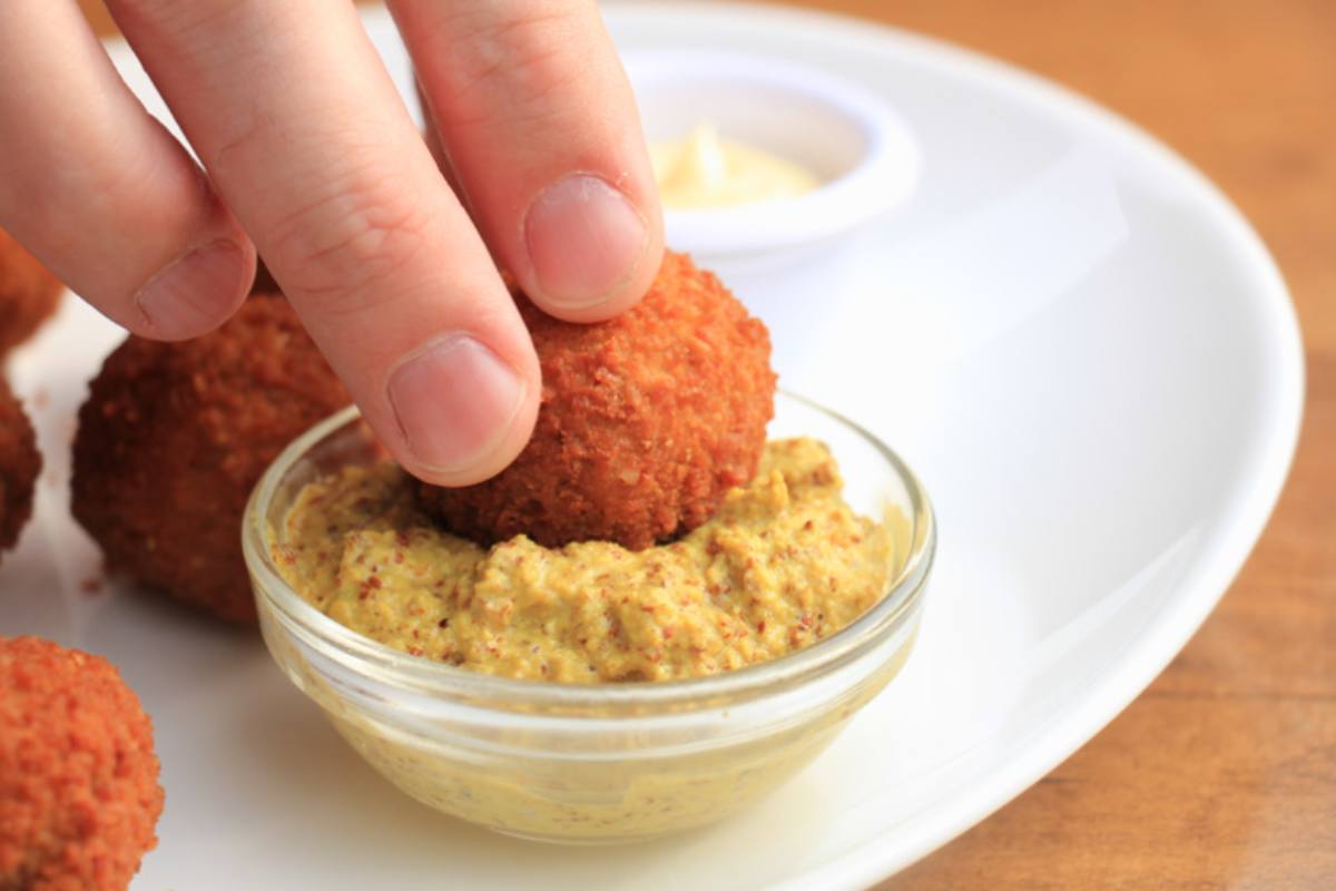 mano che immerge una polpetta fritta in una salsa