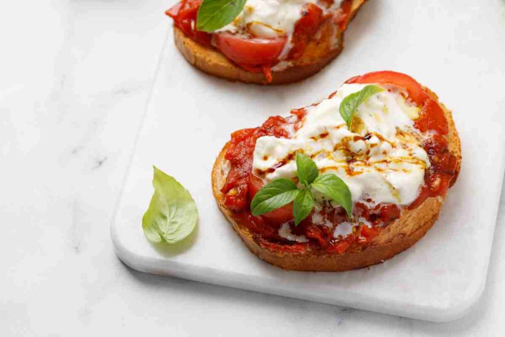 Bruschetta con alici pomodoro e stracciatella su un tagliere