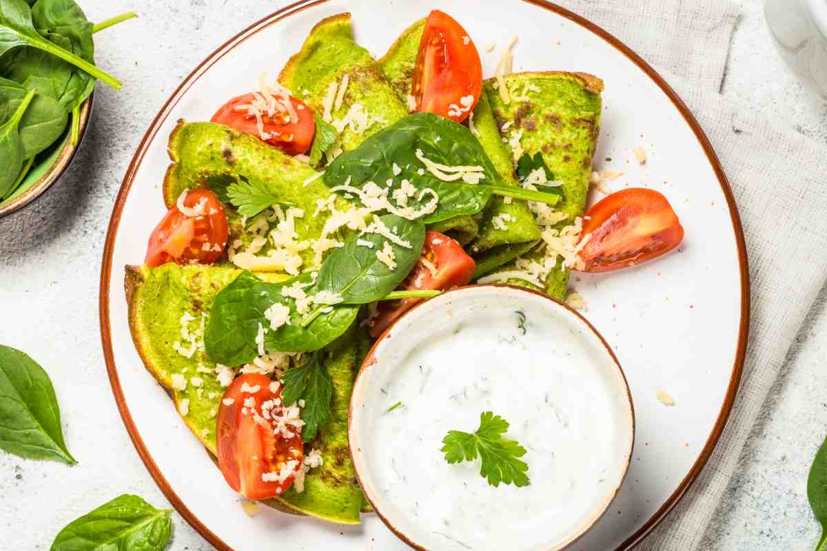 Crepes di spinaci con avocado e pomodori in un piatto visto dall'alto