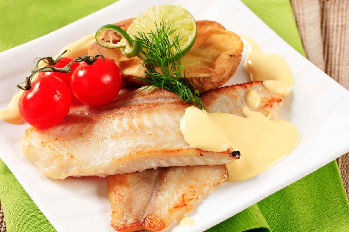 Filetti di galinella cotti in padella adagiati su un piatto quadrato con contorno di pomodorini e patate