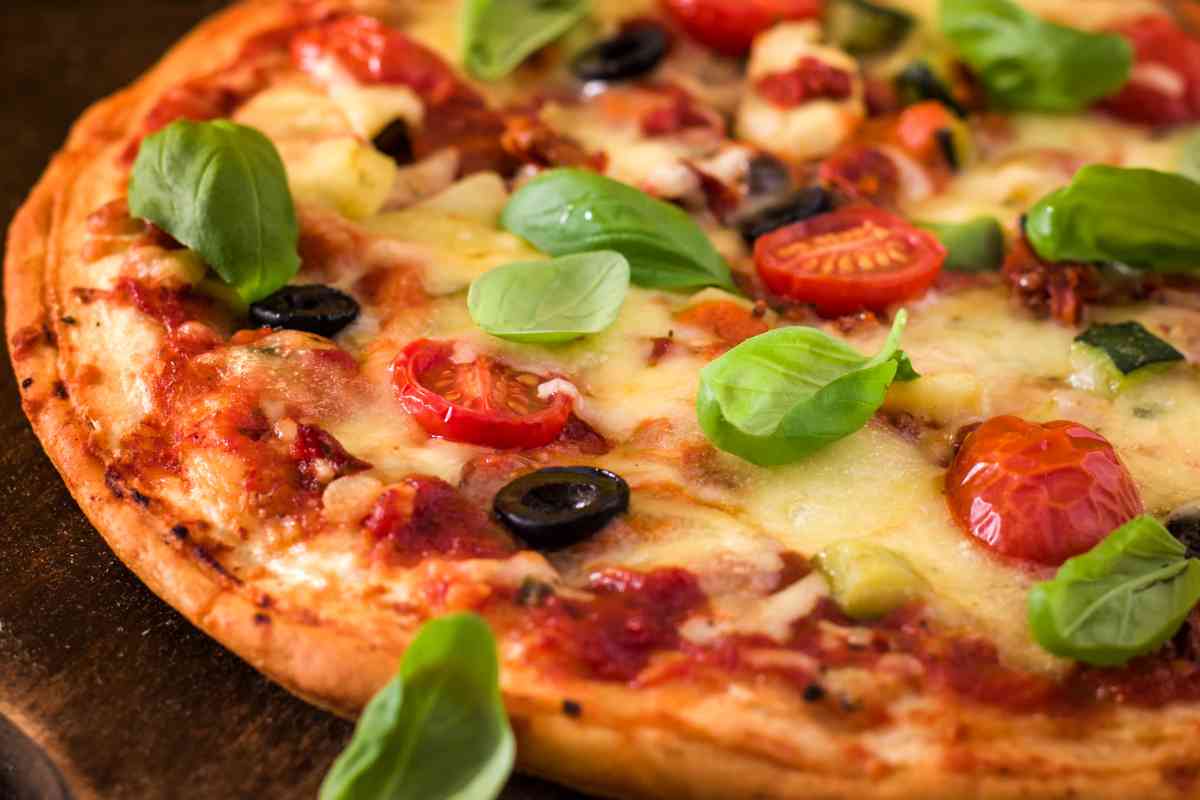 Una pizza con mozzarella, olive, basilico e pomodoro
