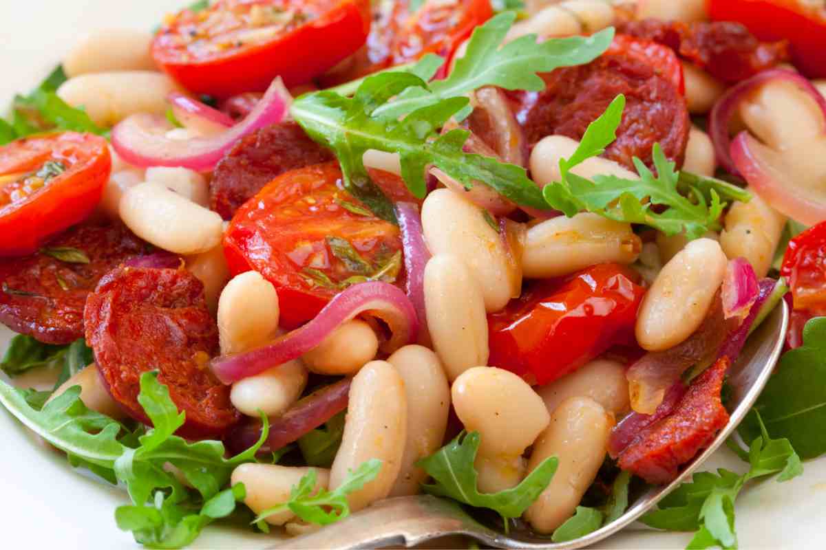 piatto con insalata di fagioli cannellini, pomodorini freschi e secchi, cipolla e rucola