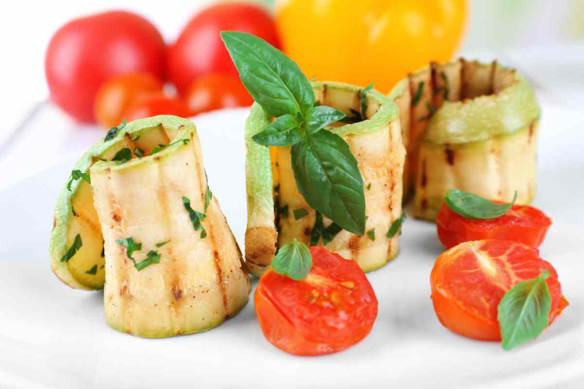 Involtini di zucchine grigliate in un piatto guarnite con pomodorini