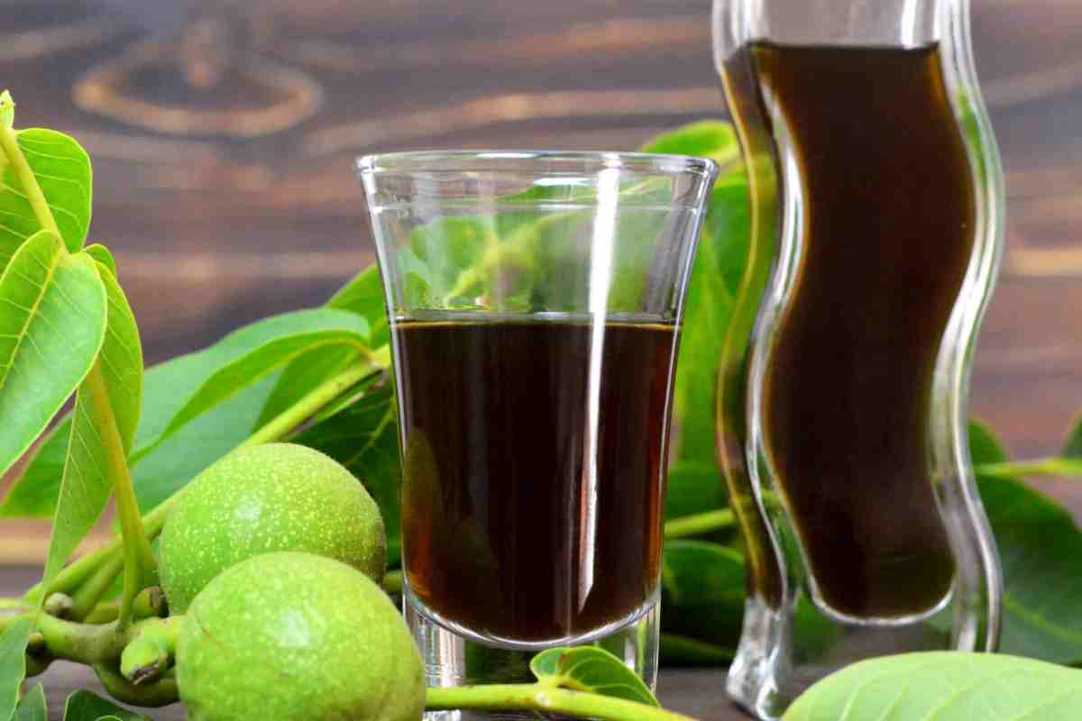 bicchiere e bottiglia con liquore nocino tra malli di noci