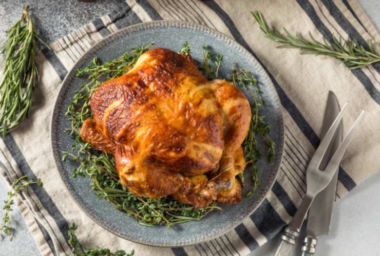 Pollo intero in un piatto con rametti di rosmarino e posate accanto