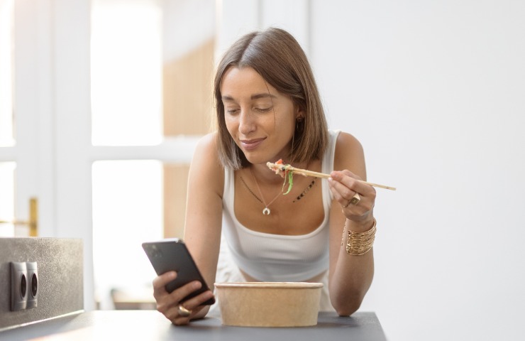 Donna che pranza consultando uno smartphone