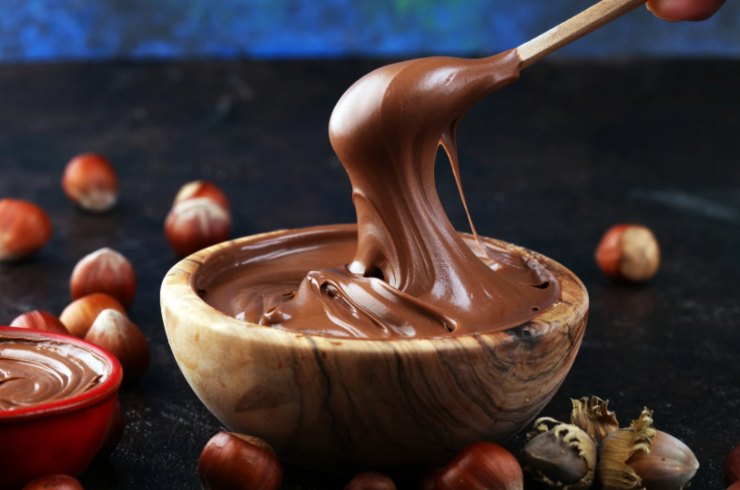 ciotola piena di crema spalmabile al cioccolato circondata da nocciole