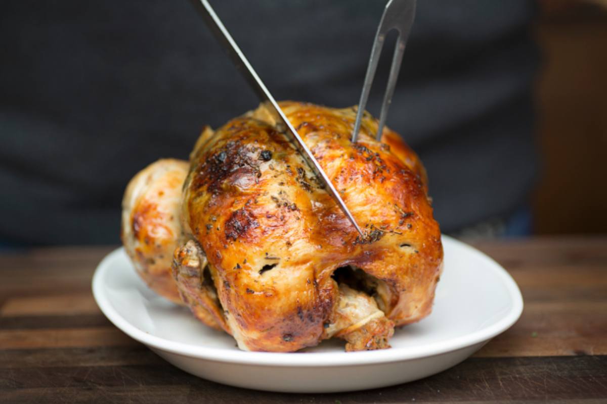 Posate che tagliano un pollo adagiato su un piatto