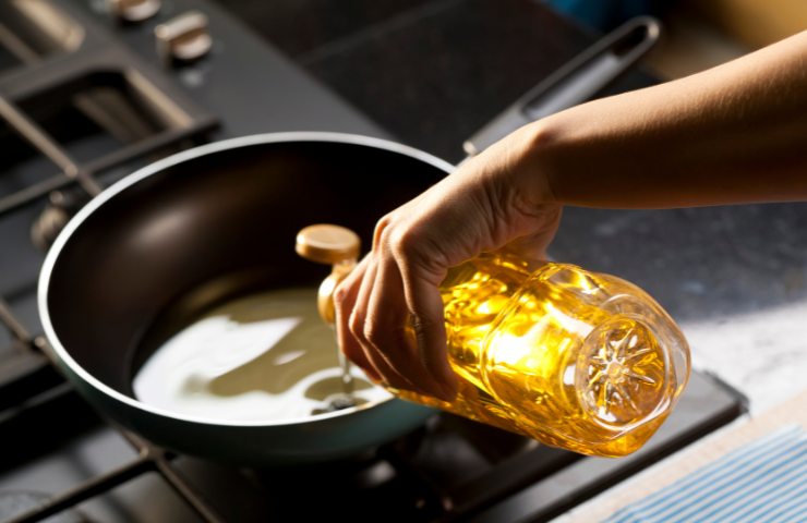 Una persona che versa olio di semi in una padella