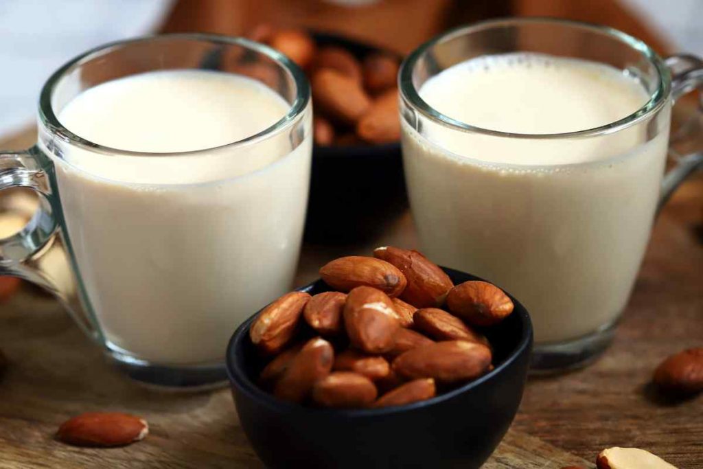 due bicchieri con Latte di mandorle fatto in casa con la ricetta virale e mandorle in una ciotola
