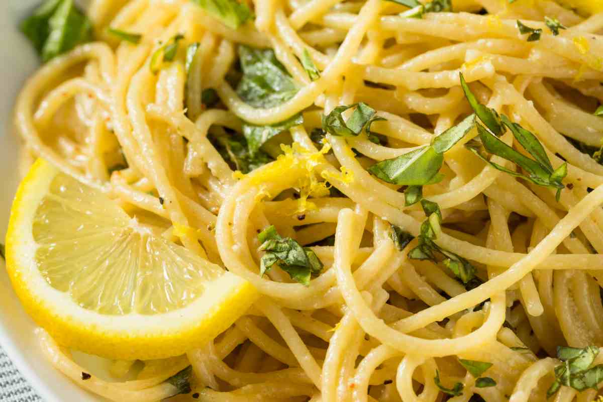 Spaghetti al limone con fetta di agrume e foglie di basilico in un piatto