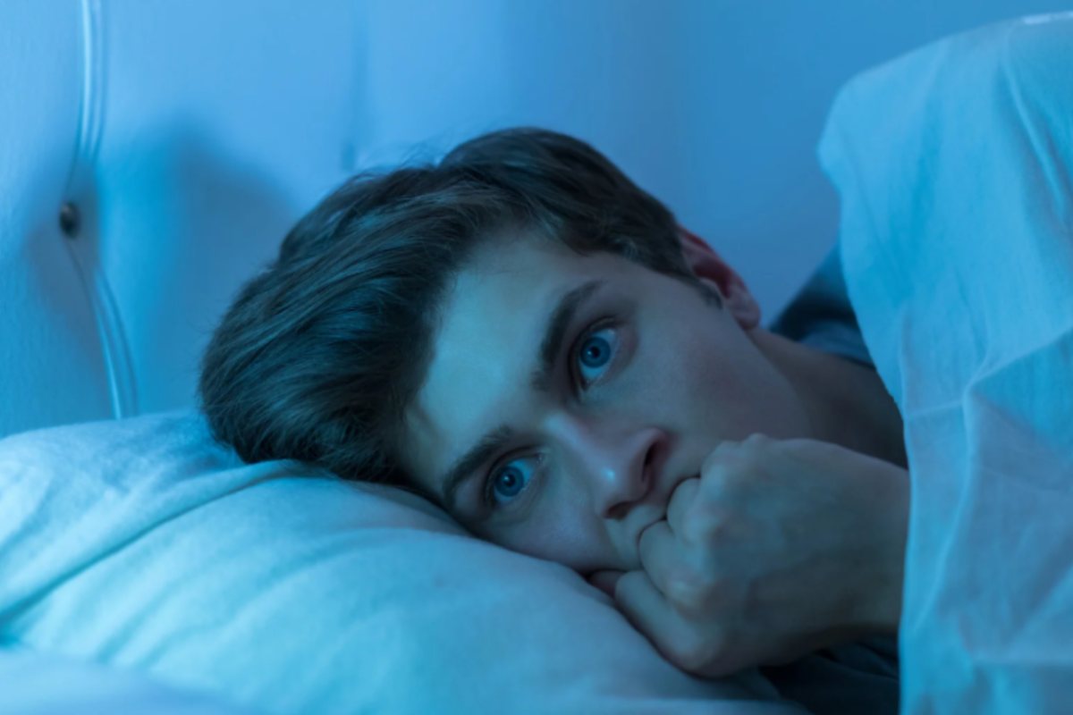uomo a letto con gli occhi spalancati che si mordi una mano